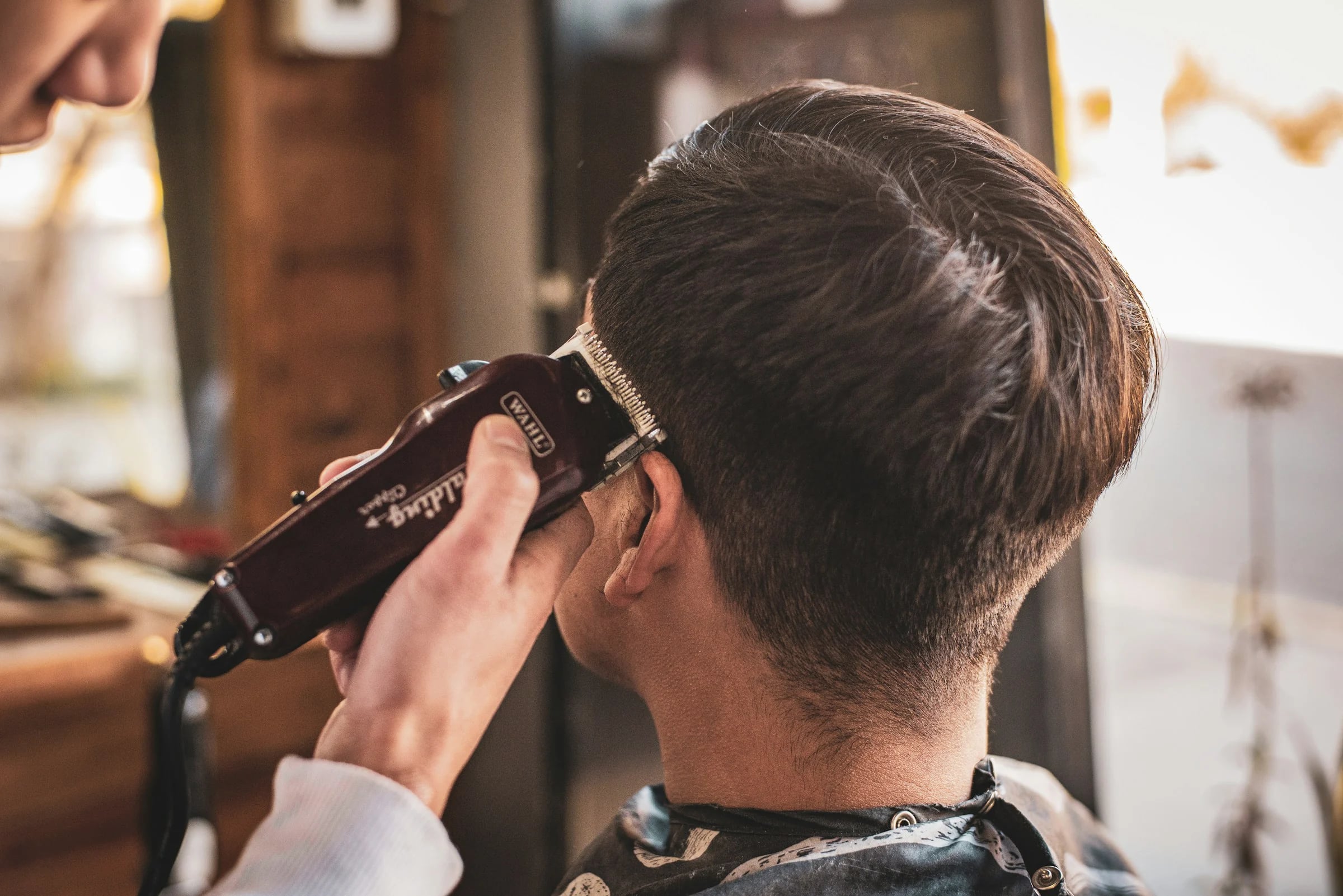 A barber taking a fade up the side of a client’s head with clippers.