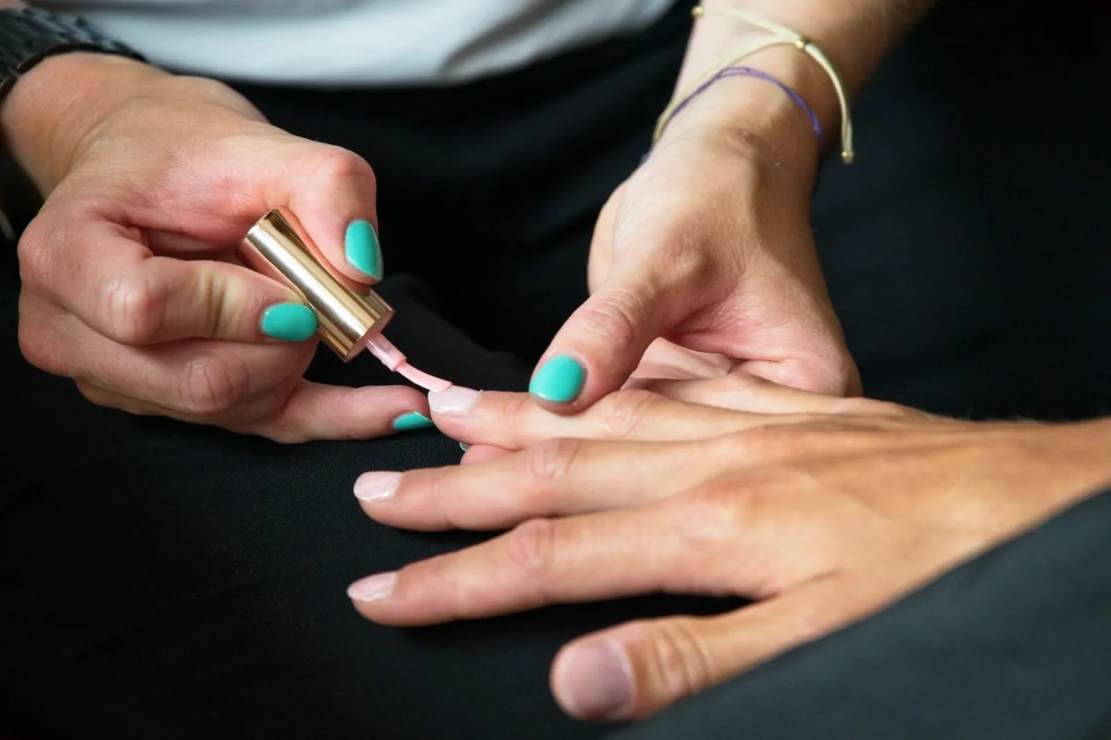 A nail technician painting a client’s nails a soft pink.